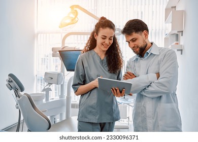 Two dentist doctors are standing in a dental office and looking at a tablet. Medicine, dentistry.Sunlight. - Powered by Shutterstock