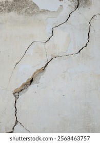 Two diagonal cracks on old white worn concrete wall. Earthquake effects. Selective focus.