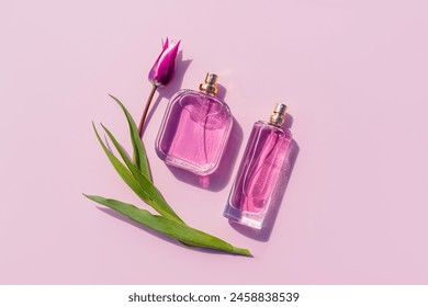 Two different bottles of perfume or eau de toilette on a lilac background with a tulip. Top view. Beauty concept. Presentation of the fragrance
