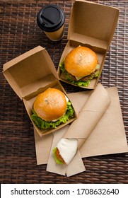 two different burgers in boxes and chicken roll with vegetables on a paper sheet. vertical view.