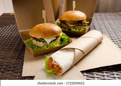 two different burgers in boxes and chicken roll with vegetables on a paper sheet.
