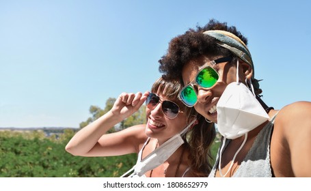 Two different race pretty young women, with a temporally removed face mask hanging from their ear, take a self portrait in a summer day. - Powered by Shutterstock