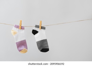 Two Different Socks Hanging On Rope Against Grey Background