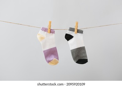 Two Different Socks Hanging On Rope Against Grey Background