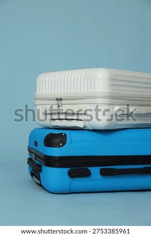 Two different stylish suitcases on light blue background, closeup