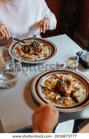 Two diners enjoy beautifully plated gourmet meals at a restaurant table with water, lemon, and elegant tableware, capturing a relaxed fine dining experience