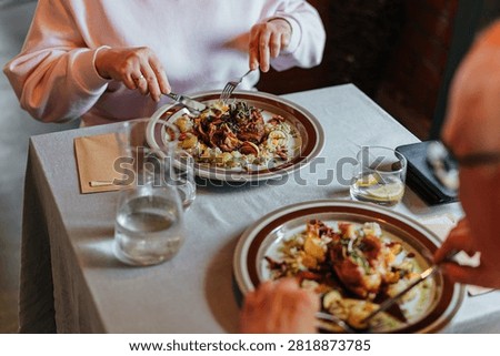 Two diners enjoy beautifully plated gourmet meals at a restaurant table with water, lemon, and elegant tableware, capturing a relaxed fine dining experience