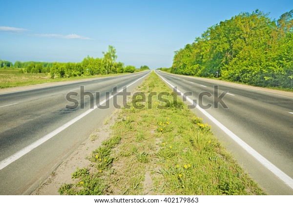 two direction of asphalt road with spring green\
grass with yellow flowers between. Transportation background. Blue\
summer sky with clouds.