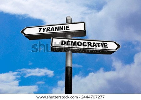 Two direction signs, one pointing left and the other one, pointing right, with written in them in French : Tyrannie  Démocratie, meaning in English: Tyranny  Democracy.