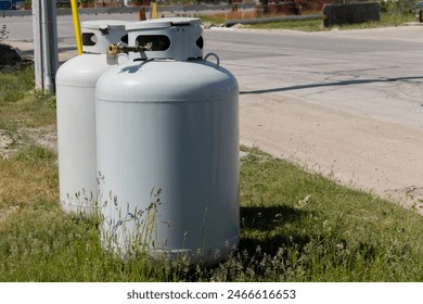 Two disconnected large vertical propane or LPG tanks resting in the grass at a construction site