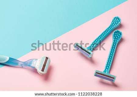 two disposable blue razors and one reusable on pink background. copy space, top view