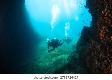 Two divers practice scuba diving skills in a rocky underwater location. Bubbles rise around them as they explore the marine environment during their training.