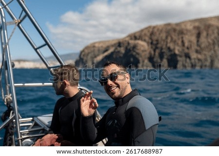 Two divers are smiling and gesturing ok sign from a boat before diving into the ocean
