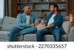 Two diverse 30s men businessmen talking at home on sofa multiracial friends companions african american caucasian ethnicity fellows brothers discussing plans friendly talk male dialogue conversation