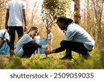 Two diverse activists working together to plant more trees and greenery, filling up ground holes and growing vegetation. Kid and teenager girls collaborating on preserving the environment.