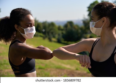 Two Diverse African And Indian Fit Ladies Friends Wear Face Masks Give Elbow Bump. Sporty Young Women Non-contact Greeting Together Outdoor Meeting For Fitness Training Or Running Outside. Closeup.