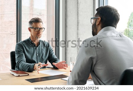 Two diverse business executive partners negotiating at board meeting, manager adviser consulting client discussing financial partnership contract sitting at table in office. Job interview concept.