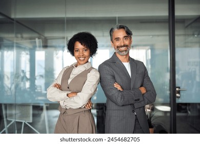 Two diverse business partners, employees or executives team standing in office arms crossed looking at camera. Business man and woman sales managers, company workers, professionals corporate portrait. - Powered by Shutterstock