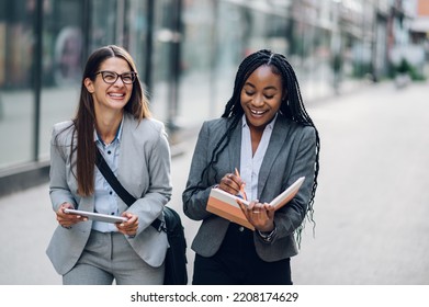 Two Diverse Business Woman Meeting Outside Of The Office. African American Female Project Manager Standing Outside The Office Building And Discussing Work With Her Caucasian Coworker. Copy Space.