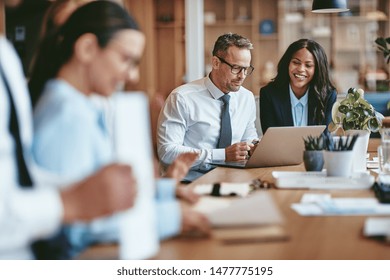 Two Diverse Businesspeople Smiling While Working On A Laptop Together At The End Of A Boardroom Table In An Office