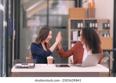 Two diverse businesswomen excitedly raise their hands happy about good news about collaboration on digital tablets and laptops in the office. - Powered by Shutterstock