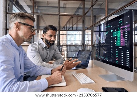 Two diverse crypto traders brokers stock exchange market investors discussing trading charts research reports growth using pc computer looking at screen analyzing invest strategy, financial risks.