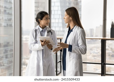 Two diverse doctor women using tablet, discussing medical case, electronic records, online healthcare service, holding digital gadget, talking, consulting each other - Powered by Shutterstock