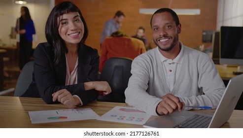 Two Diverse Employees At Work. An African Man Talking With A Hispanic Female Brazilian Colleague In Front Of Laptop Computer