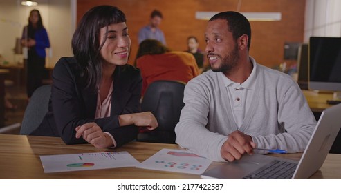 Two Diverse Employees At Work. An African Man Talking With A Hispanic Female Brazilian Colleague In Front Of Laptop Computer