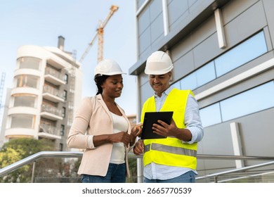 Two diverse Engineer and architect using tablet discussing building project at construction site