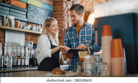 Two Diverse Entrepreneurs Have A Team Meeting In Their Stylish Coffee Shop. Barista And Cafe Owner Discuss Work Schedule And Menu On Tablet Computer. Young Female And Male Restaurant Employees.