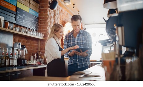 Two Diverse Entrepreneurs Have a Team Meeting in Their Stylish Coffee Shop. Barista and Cafe Owner Discuss Work Schedule and Menu on Tablet Computer. Young Female and Male Restaurant Employees. - Powered by Shutterstock