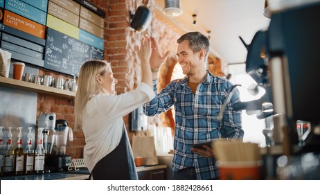 Two Diverse Entrepreneurs Have a Team Meeting in Their Stylish Coffee Shop. Barista and Cafe Owner Discuss Work Schedule and Menu on Tablet Computer. Young Female and Male Give Each Other High Five. - Powered by Shutterstock