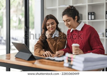 Two diverse female smiling while working together at a boardroom table during a meeting in a modern office