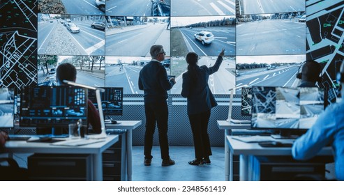 Two Diverse Male and Female Software Engineers Discuss Live Analysis Feed with City Road and Traffic Updates. Managers and Data Scientists Collaborate in a Modern Monitoring Office - Powered by Shutterstock