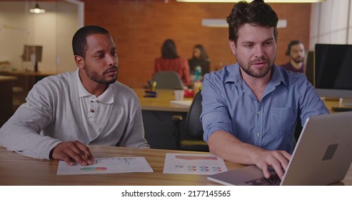 Two Diverse Millennial Employees In Front Of Laptop. A Black Colleague Explains New Job For A South American Female Employee. First Day At New Job Concept