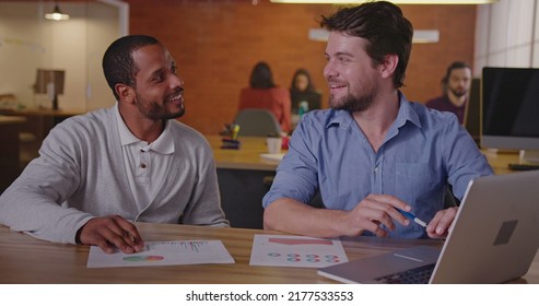 Two Diverse Millennial Employees In Front Of Laptop. A Black Colleague Explains New Job For A South American Female Employee. First Day At New Job Concept