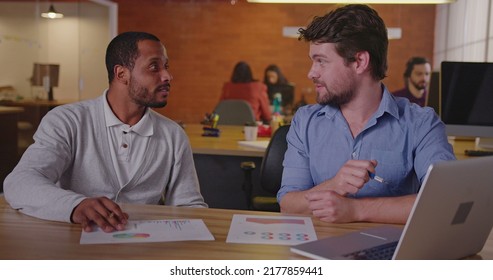 Two Diverse Millennial Employees In Front Of Laptop. A Black Colleague Explains New Job For A South American Female Employee. First Day At New Job Concept