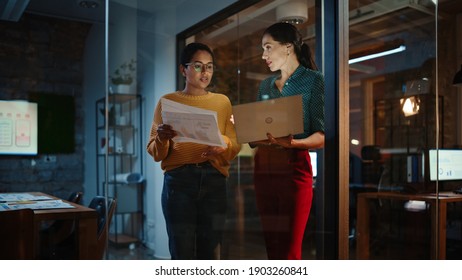 Two Diverse Multiethnic Women Have a Conversation in a Meeting Room Behind Glass Walls in an Agency. Creative Director and Project Manager Talk About Business Results and App Designs in an Office.