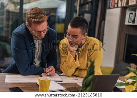 Two diverse natural colleagues in casual office or home office doing paperwork working together teaching, coaching or tutoring each other one another