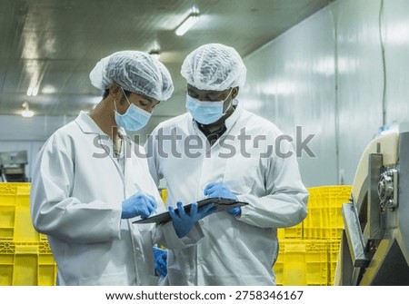 Two diverse quality control inspectors in protective gear discussing production data on a clipboard in a food manufacturing plant to maintain global compliance and operational excellence.