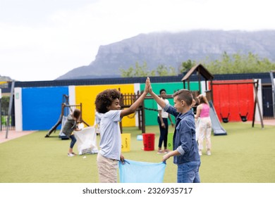 Two diverse schoolboys collecting rubbish for recycling high fiving in schoolyard, with copy space. Education, inclusivity, elementary school and learning concept. - Powered by Shutterstock