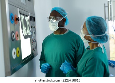 Two diverse surgeons discussing x-ray on lightbox in operating theatre. Hospital, medical and healthcare services.