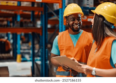 Two diverse warehouse workers are smiling and discussing logistics while holding a clipboard, showcasing teamwork and efficiency in a vibrant warehouse setting - Powered by Shutterstock