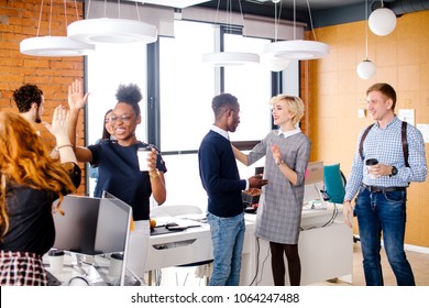 two diverse women are making high five, Caucasian man is looking at talking woman with fair hair with African man in break time - Shutterstock ID 1064247488
