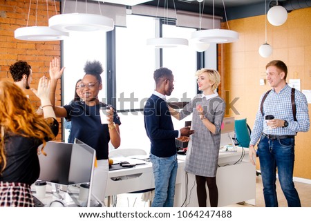two diverse women are making high five, Caucasian man is looking at talking woman with fair hair with African man in break time