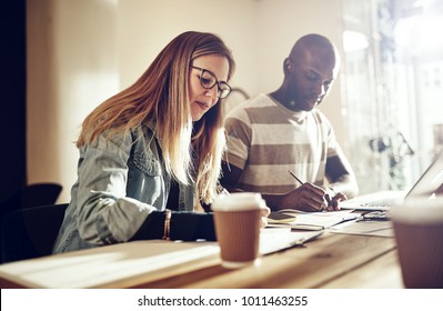 Two diverse work colleagues writing down notes while working together at a table in a modern office  - Shutterstock ID 1011463255