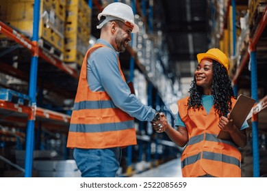 Two diverse workers in safety gear share a handshake in a warehouse, symbolizing successful collaboration, agreement, and mutual respect in an industrial setting. - Powered by Shutterstock