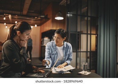 Two Diverse Young Businesswomen Discussing Work Together While Working Late At A Table In An Office