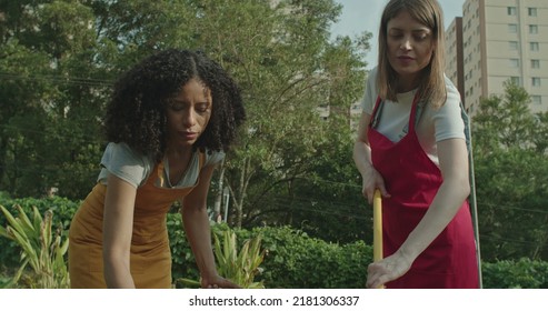 Two Diverse Young Women Working At Farm Treating The Soil. Farming Workers At Urban City Farm